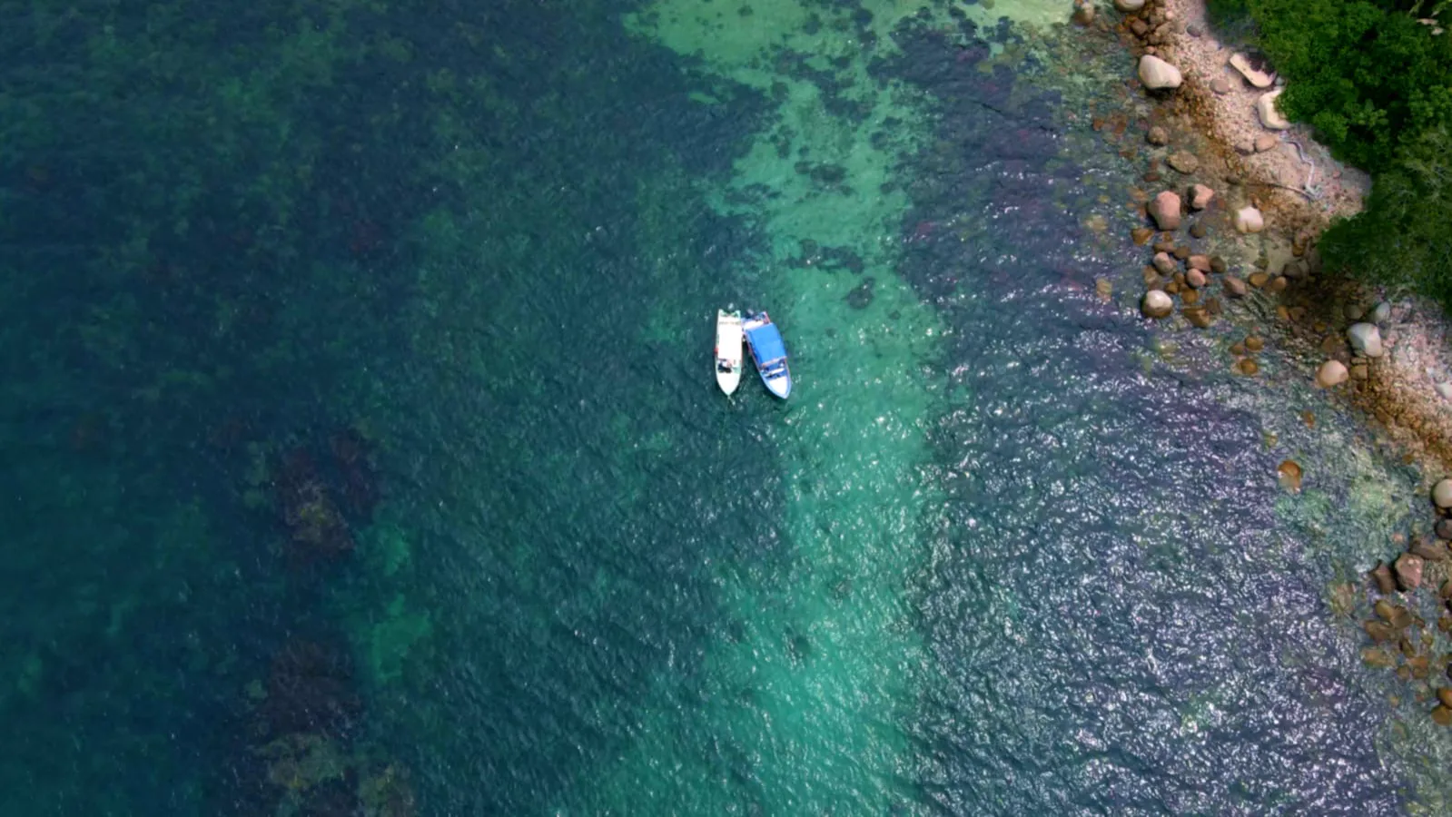 Two safari boats floating over turquoise water beside a rocky tropical coast